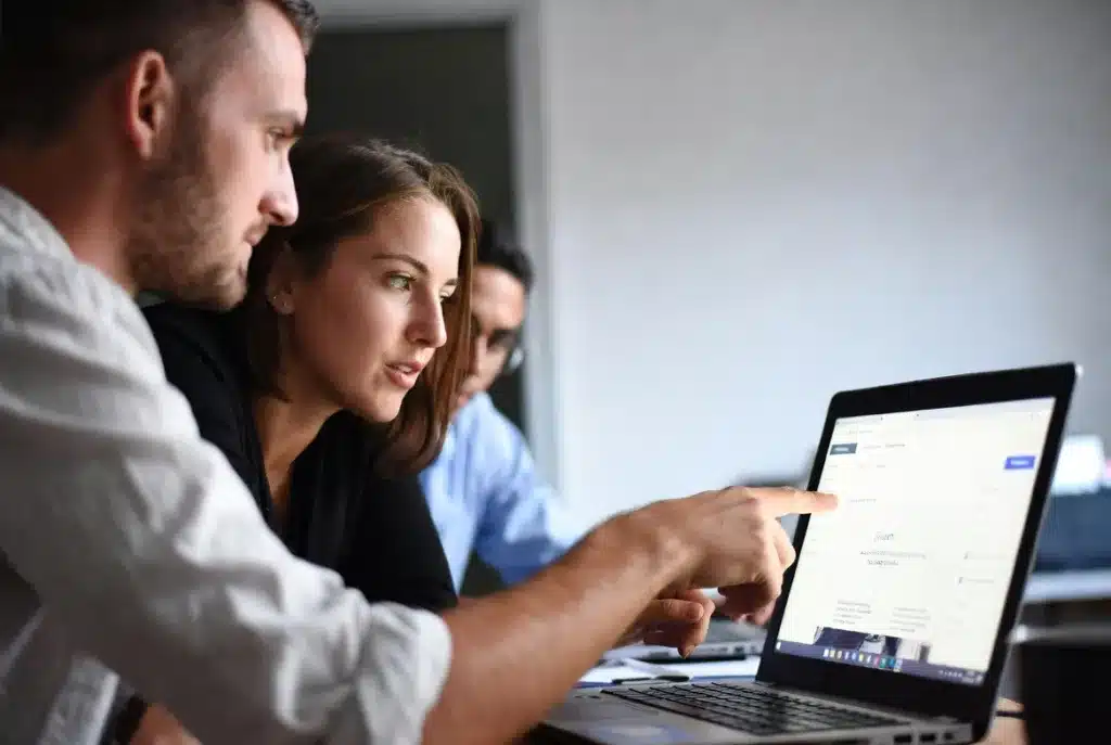 A small marketing team of two or three people gathered around a laptop, pointing at a website on screen. Casual but professional setting. One person appears to be making an edit or publishing something. The energy is collaborative and autonomous, not waiting on anyone.