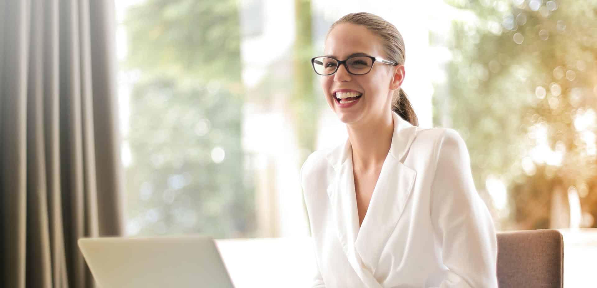 A businesswoman sitting and wearing a white suit checks digital marketing results on a laptop